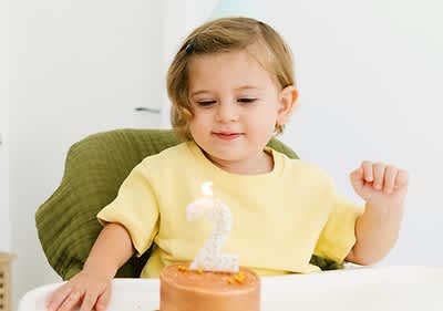 Kleines Mädchen sitzt vor Geburtstagstorte zum 2. Geburtstag