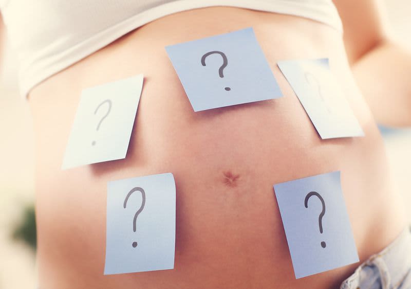 Schwangerer Bauch beklebt mit Zetteln auf welchen Fragezeichen stehen