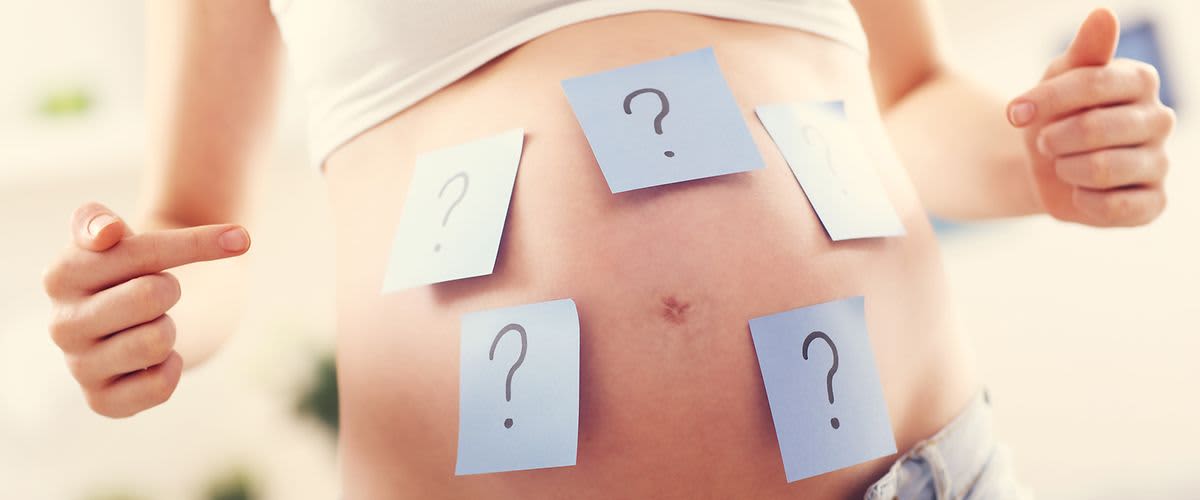 Schwangerer Bauch beklebt mit Zetteln auf welchen Fragezeichen stehen