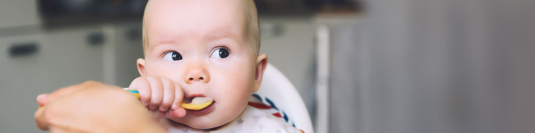 Baby hat Löffel in der Hand und führt ihn zum Mund
