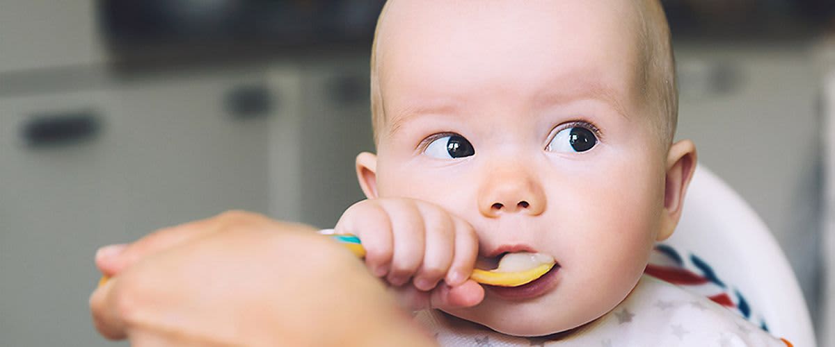 Baby hat Löffel in der Hand und führt ihn zum Mund