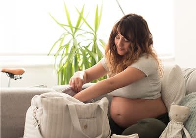 Schwangere Frau hat Babykleidung in den Händen