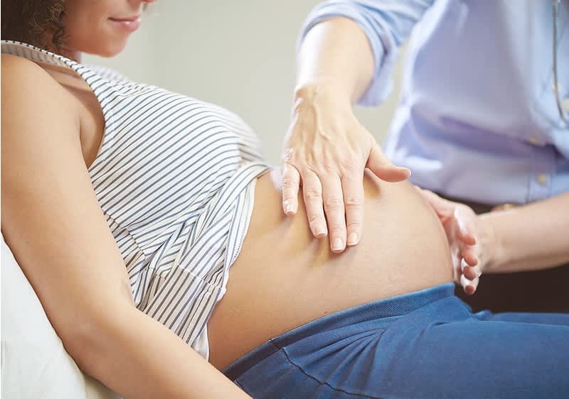 Hebamme tastet den Bauch einer schwangeren Frau mit beiden Händen ab.