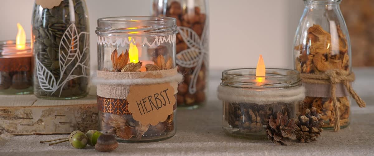 Dekorierte Gläser mit Herbstmotiven und Kerzenlicht