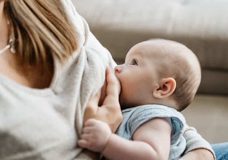 Mutter legt Neugeborenes an die Brust an und stillt das Baby.