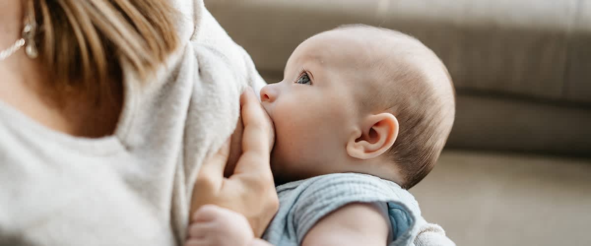 Mutter legt Neugeborenes an die Brust an und stillt das Baby.