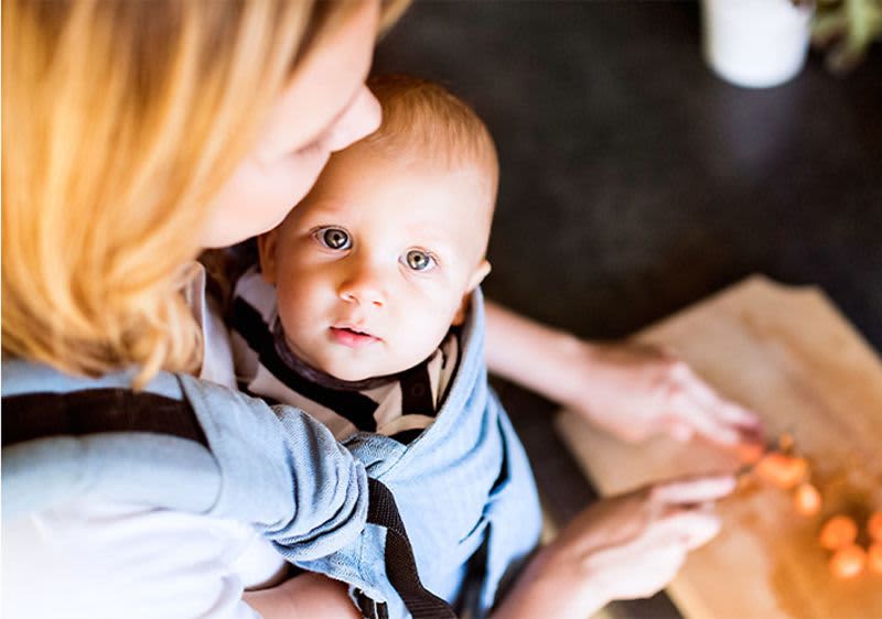 Frau mit Baby in der Trage schneidet Gemüse