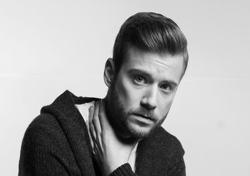 Dunkelhaariger Mann mit 3-Tage-Bart hat die linke Hand um den Hald gelegt.