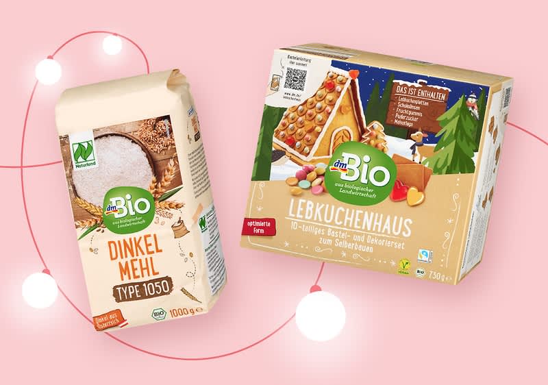 Zwei Produktverpackungen vor einem rosa Hintergrund mit Lichterkette. Links eine Packung Dinkelmehl Typ 1050 von dmBio mit einem Bild von Mehl und einem Holzlöffel. Rechts eine Verpackung für ein Lebkuchenhaus von dmBio mit Abbildungen von Lebkuchen, einem Weihnachtsbaum und einem Schneemann.