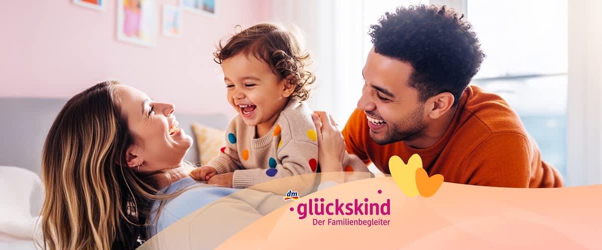 Ein Kleinkind mit einem bunten Pullover sitzt auf dem Bauch einer liegenden Frau, während ein Mann sich zu ihnen beugt. Unten rechts das Logo von dm glückskind, Der Familienbegleiter.. Bild mithilfe von KI erstellt