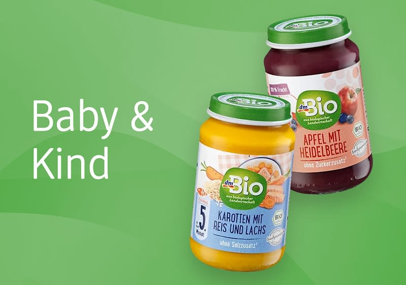 Zwei Gläser mit Babynahrung auf grünem Hintergrund, links ein gelbes Glas mit der Aufschrift „Karotten mit Reis und Lachs“, rechts ein rotes Glas mit der Aufschrift „Apfel mit Heidelbeere“, daneben der Text „Baby & Kind“