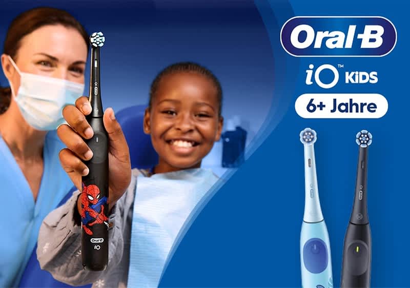 Zwei Personen halten jeweils eine Oral‑B iO Kinderzahnbürste, vorn eine schwarze Zahnbürste mit Spiderman‑Motiv, rechts neben ihnen zwei weitere Bürsten abgebildet in hellblau und dunkelgrau sowie Schriftzug „Oral‑B iO KIDS 6+ Jahre“ auf blauem Hintergrund