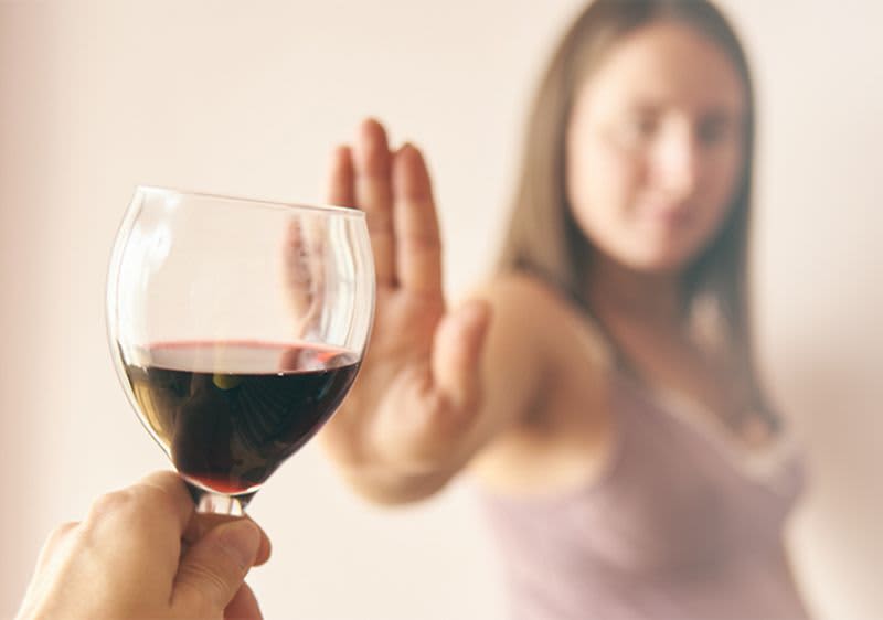 Frau wehrt mit der Hand ein Glas Wein ab