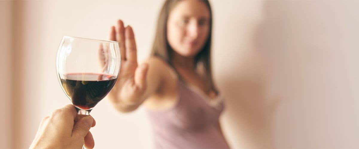 Frau wehrt mit der Hand ein Glas Wein ab