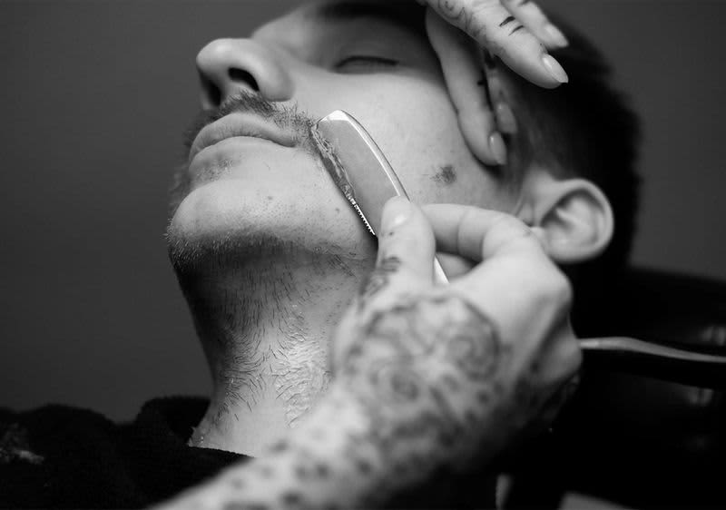 Barber rasiert die Wange eines Mannes mit dem Rasiermesser