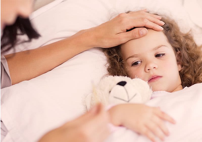 Mutter legt ihre Hand auf die Stirn des kranken Kindes