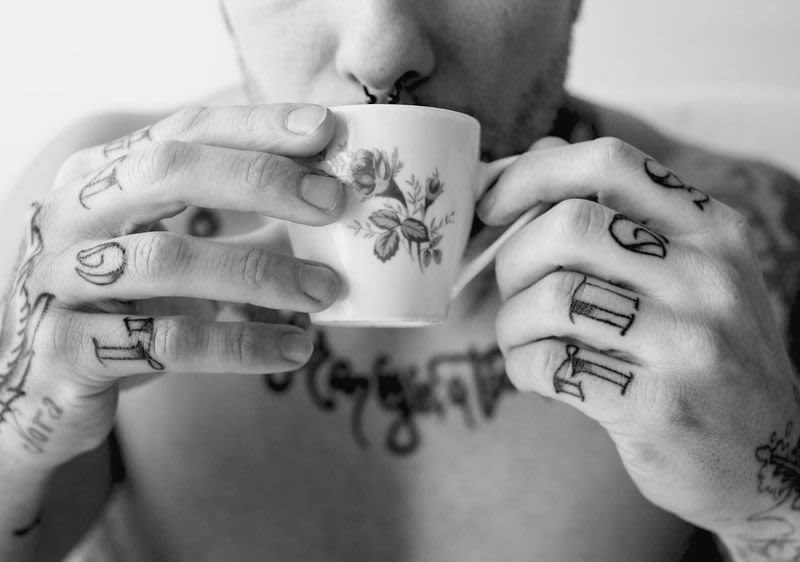Tätowierter Mann mit Nasenring trinkt aus einer geblümten Tasse.