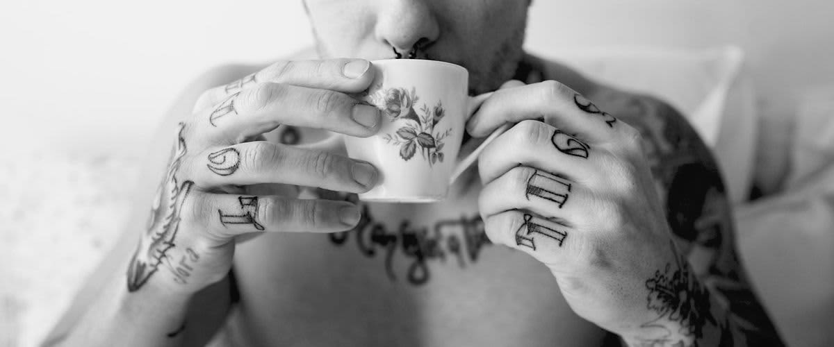 Tätowierter Mann mit Nasenring trinkt aus einer geblümten Tasse.