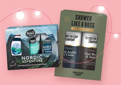 Zwei Produktverpackungen nebeneinander, links eine Balea Men Geschenkbox mit Duschgel, Bodylotion und Crew-Socken, Aufschrift „Nordic Adventure“, rechts eine Brooklyn Soap Company Geschenkbox mit zwei Duschgels, Aufschrift „Shower Like a Boss“ und „Blue Amber & Cedar“ sowie „Oud Wood & Sandal“