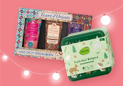 Eine Geschenkbox mit drei Tesori d'Oriente Pflegeprodukten und der Aufschrift „Lass dich verzaubern“ neben einer grünen alverde Geschenkbox mit der Aufschrift „Gepflegtes Waldglück Pflegedusche“ auf einem rosa Hintergrund mit weißen Lichterketten
