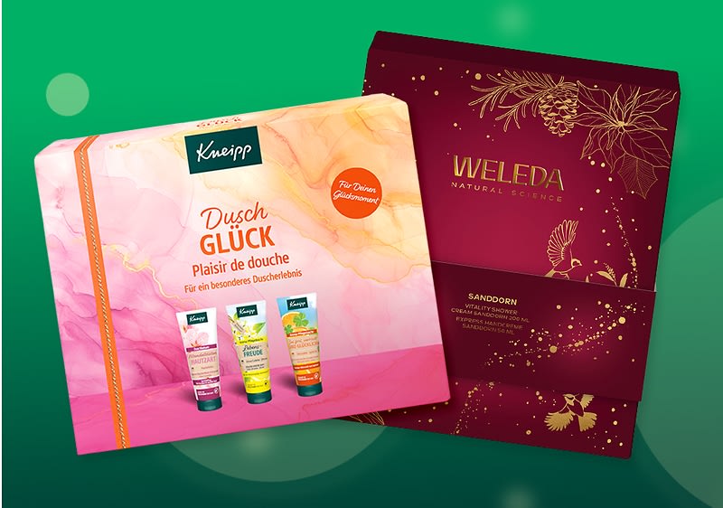 zwei Geschenkpackungen mit Duschpflege: links rosa-orangene Schachtel der Marke Kneipp mit der Aufschrift „Dusch GLÜCK“ und Abbildungen dreier Duschgele, rechts dunkelrote Weleda-Geschenkbox mit goldfarbenen Illustrationen und der Aufschrift „WELEDA“