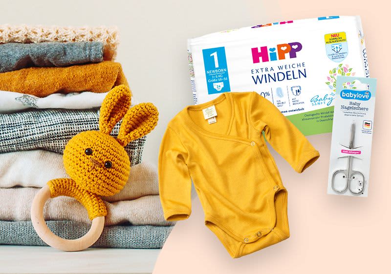 Schwangere Frau steht vor Babykleidung