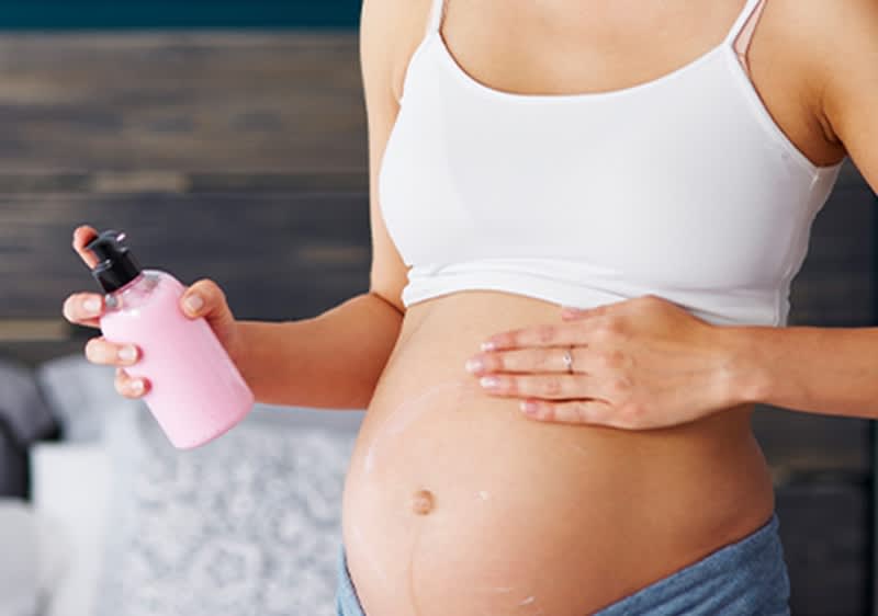 Werdende Mutter beugt Schwangerschaftsstreifen durch Massage mit Lotion vor.