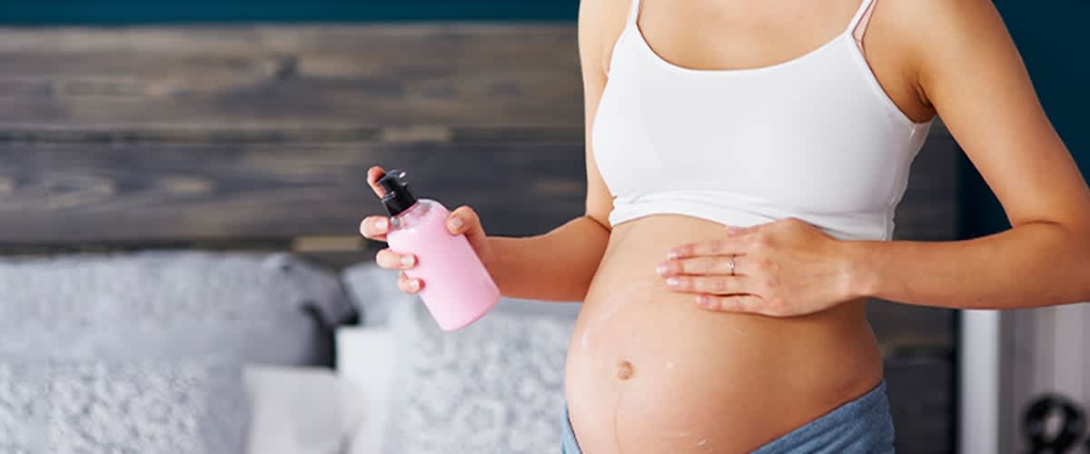Werdende Mutter beugt Schwangerschaftsstreifen durch Massage mit Lotion vor.