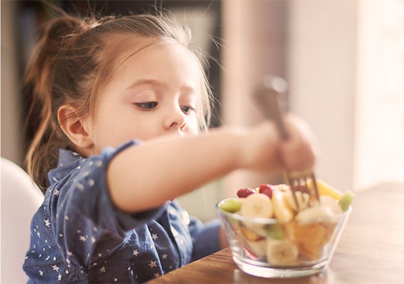 Kind sticht mit einer Gabel in den Obstsalat