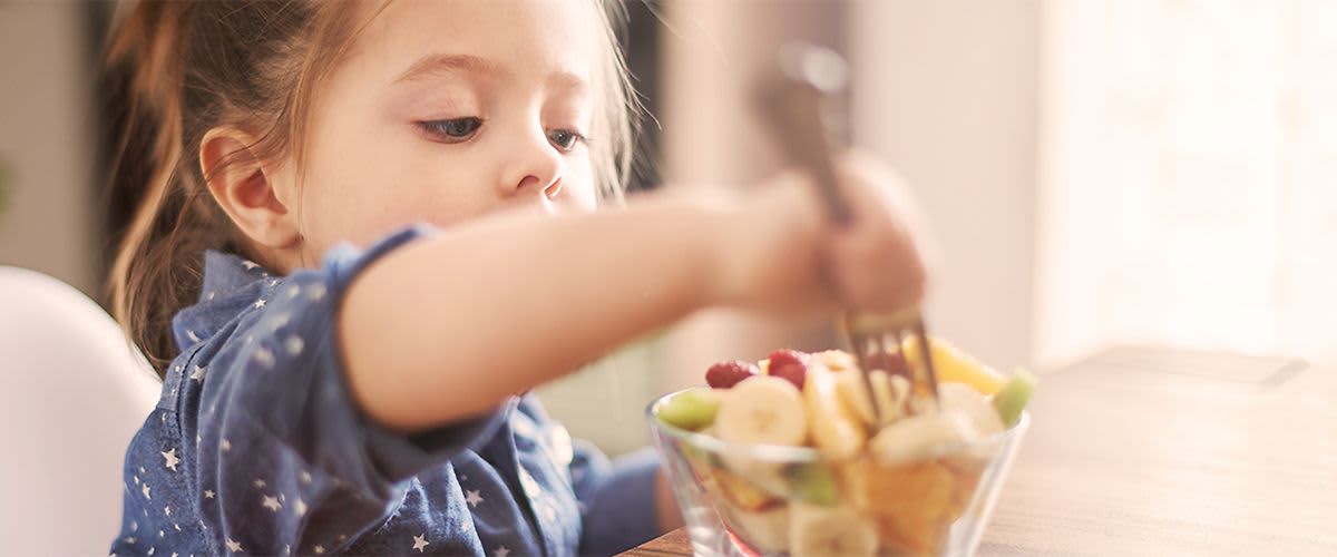 Kind sticht mit einer Gabel in den Obstsalat