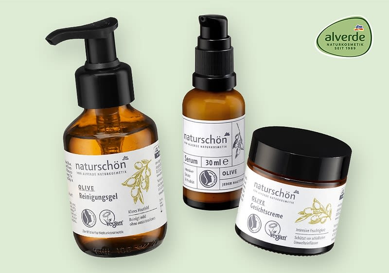 Drei Produkte der Marke Alverde Naturkosmetik: ein Oliven-Reinigungsgel in einer Pumpflasche, ein Oliven-Serum in einer kleinen Flasche mit Sprühkopf und eine Oliven-Gesichtscreme in einem Tiegel. Alle Produkte tragen das Vegan-Logo und sind mit Olivenmotiven gestaltet.
