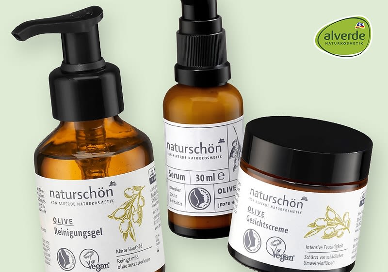 Drei Produkte der Marke Alverde Naturkosmetik: ein Oliven-Reinigungsgel in einer Pumpflasche, ein Oliven-Serum in einer kleinen Flasche mit Sprühkopf und eine Oliven-Gesichtscreme in einem Tiegel. Alle Produkte tragen das Vegan-Logo und sind mit Olivenmotiven gestaltet.