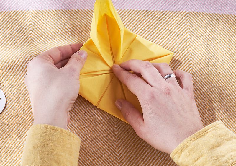 Halten der Serviette in der Mitte und rundes ausformen der äußeren Ecke