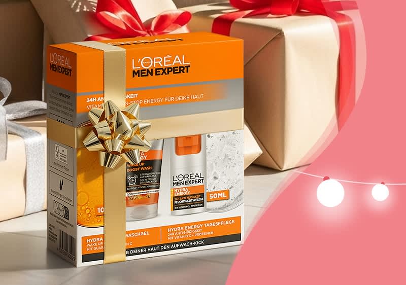 Eine Geschenkbox von L'Oréal Men Expert mit einer goldenen Schleife, enthält ein Duschgel und eine Gesichtspflege, Aufschrift „24H Frischekick“ und „Hydra Energy“ auf orangefarbenem Hintergrund, daneben zwei verpackte Geschenke mit roten Schleifen