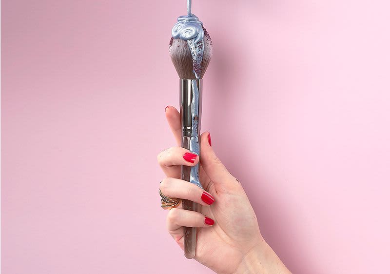 Hand mit rotem Nagellack und Make-up Pinsel 