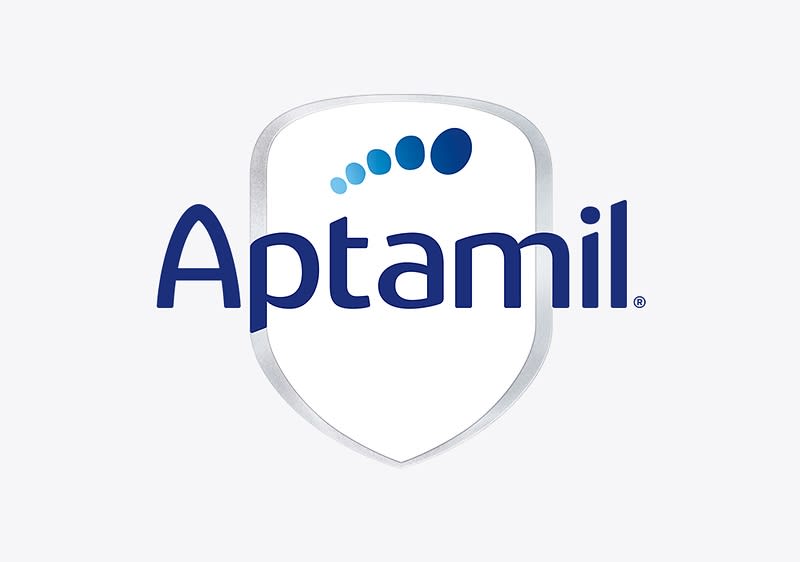Das Bild zeigt das Logo der Marke Aptamil, bestehend aus einem weißen Schild mit einem silbernen Rand, auf dem der Schriftzug Aptamil in blauer Farbe zu sehen ist, darüber befinden sich fünf blaue Punkte, die in einer geschwungenen Linie angeordnet sind und von klein nach groß verlaufen