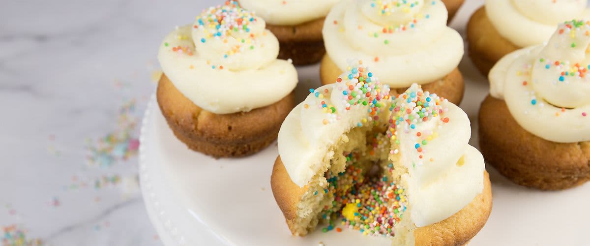 Angeschnittene Cupcakes mit weißem Topping und bunten Zuckerkugeln