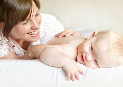 Frau streichelt über den Rücken ihres Babys im Bett