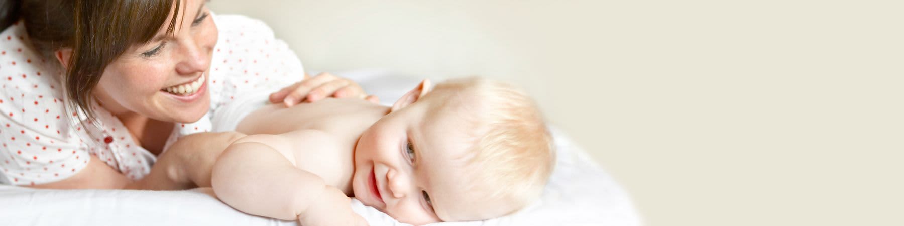 Frau streichelt über den Rücken ihres Babys im Bett