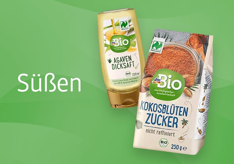 Eine grüne Verpackung mit der Aufschrift „dmBio Kokosblütenzucker nicht raffiniert“ neben einer goldenen Flasche mit der Aufschrift „dmBio Agavendicksaft“ auf grünem Hintergrund mit dem Wort „Süßen“