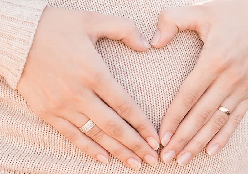 Frau formt mit ihren Händen ein Herz vor ihrem Babybauch