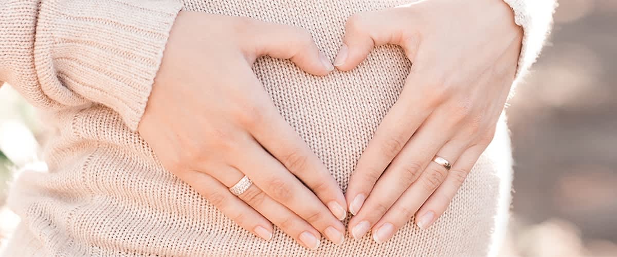 Frau formt mit ihren Händen ein Herz vor ihrem Babybauch