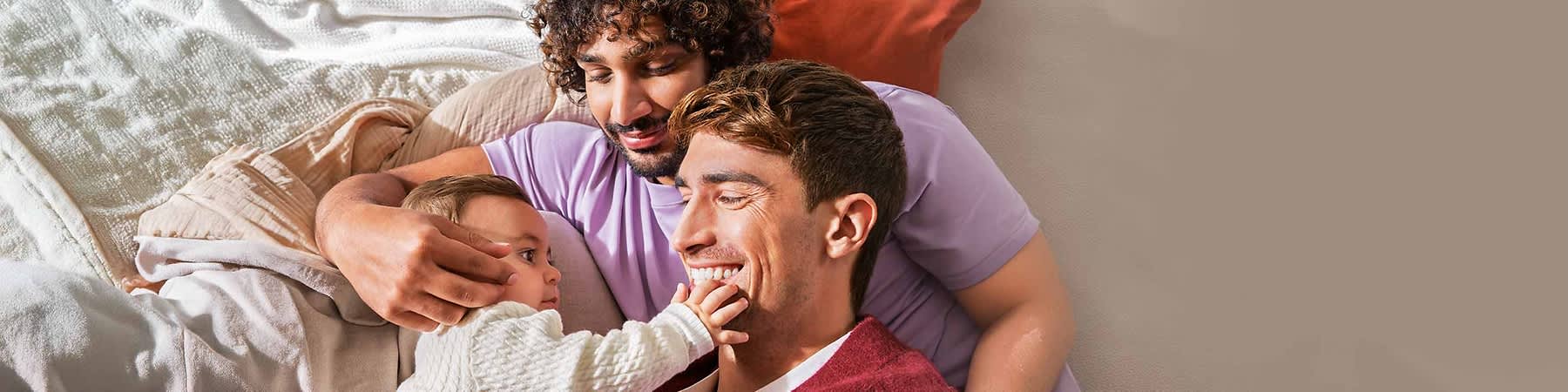 Zwei Erwachsene kuscheln mit Baby auf Sofa