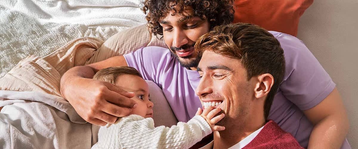 Zwei Erwachsene kuscheln mit Baby auf Sofa