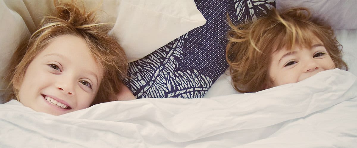 Zwei Kind liegen lachend im Bett