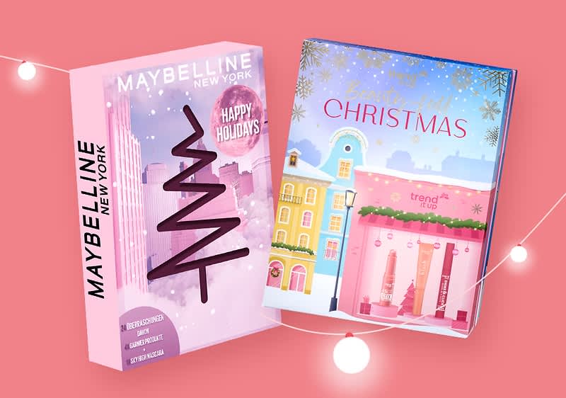 Zwei Geschenkboxen auf einem rosa Hintergrund, links eine Maybelline New York Box mit einem stilisierten Weihnachtsbaum und der Aufschrift Happy Holidays, darunter Bürstenloses Auftragen, Langanhaltend, Geschmeidig, rechts eine trend IT UP Box mit der Aufschrift Beautyful Christmas und einer Illustration von bunten Häusern mit Weihnachtsdekoration, darunter sind mehrere Lippenstifte sichtbar