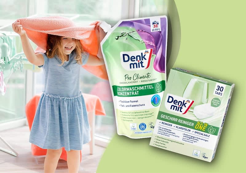 Ein kleines Mädchen im blauen Kleid hält ein großes Handtuch über den Kopf, daneben zwei Denkmit-Produkte: rechts eine grüne Box mit der Aufschrift „Denk mit Geschirr Reiniger ONE 30 Tabs“ und links eine nachfüllbare, violett-grün gestaltete Nachfüllverpackung mit der Aufschrift „Denk mit Colorwaschmittel Konzentrat“