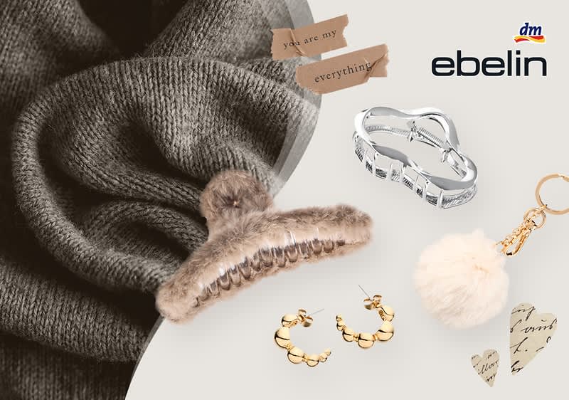 Eine Collage aus verschiedenen Accessoires und Dekorationen, darunter ein silberner Haarclip, ein goldener Ohrring in Form von Kreisen, ein Schlüsselanhänger mit einem weißen, flauschigen Pompon, getrocknete Blumen und ein Herz aus Papier mit der Aufschrift you are my everything, im Hintergrund ein grauer Wollstoff, oben rechts das Logo von ebelin und dm