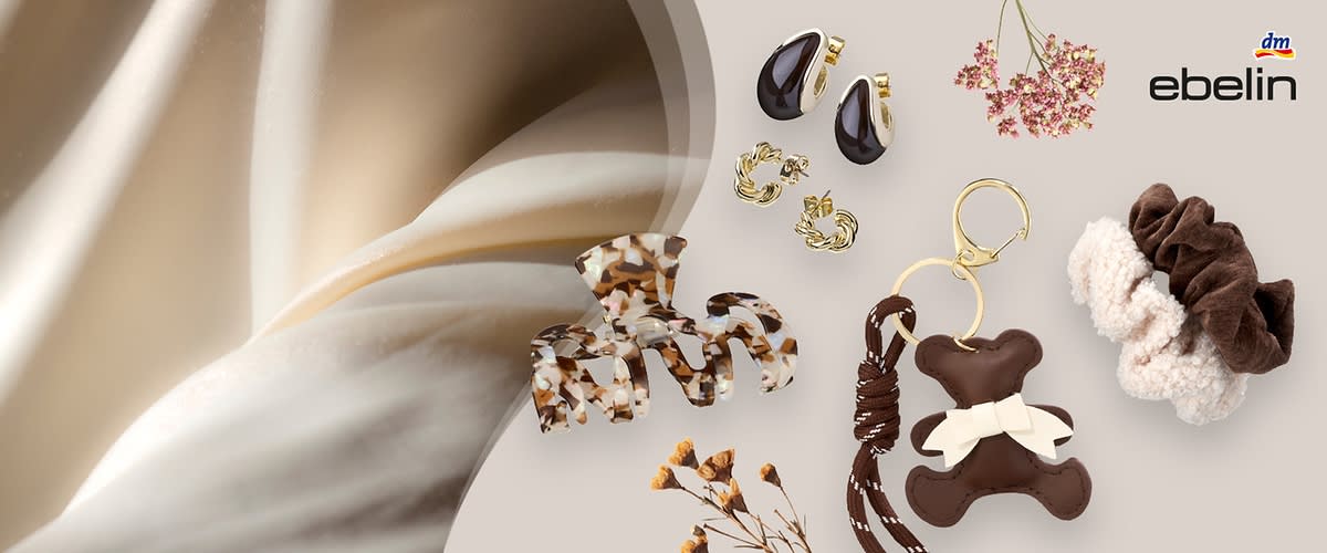 Mehrere Haaraccessoires der Marke ebelin: zwei gemusterte Haarklammern im Schildpatt-Look, zwei goldfarbene Ohrclip-Ohrringe mit dunklen Tropfen, zwei kleine goldfarbene Creolen, ein braunes und ein cremefarbenes Fleece-Scrunchie sowie ein braunes Schlüsselanhänger-Accessoire in Bärenform mit Schleife, dm-Logo oben rechts
