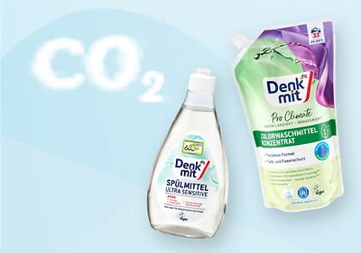 Eine Flasche Denkmit Spülmittel Ultra Sensitive und eine Packung Denkmit Pro Climate Colorwaschmittel Konzentrat auf hellblauem Hintergrund mit CO2-Schriftzug in Wolkenoptik